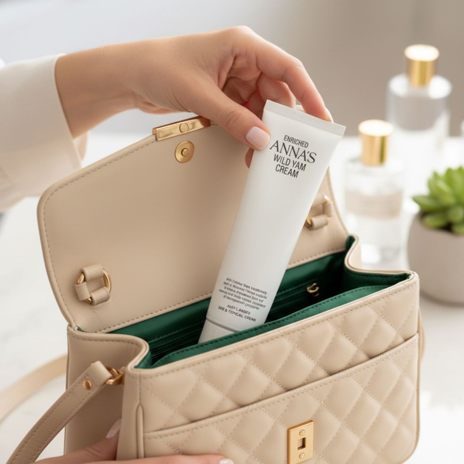 A close-up of a hand placing a tube of Enriched Anna's Wild Yam Cream into a quilted, beige leather handbag with a green interior lining