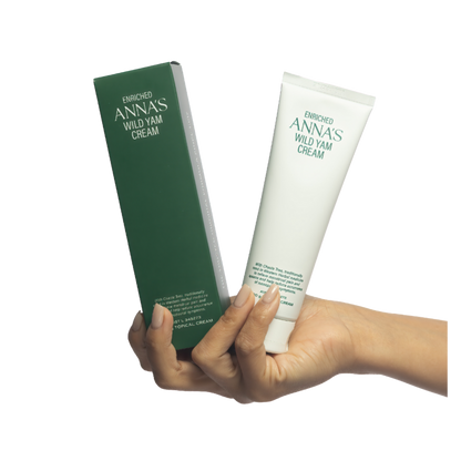 Hand holding a tube and box of Enriched Anna's Wild Yam Cream on a white background