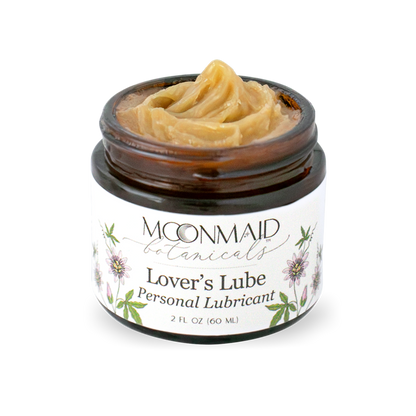 An open amber glass jar of MoonMaid Botanicals Lover's Lube Personal Lubricant, showing a thick, swirled peak of tan-colored ointment inside.