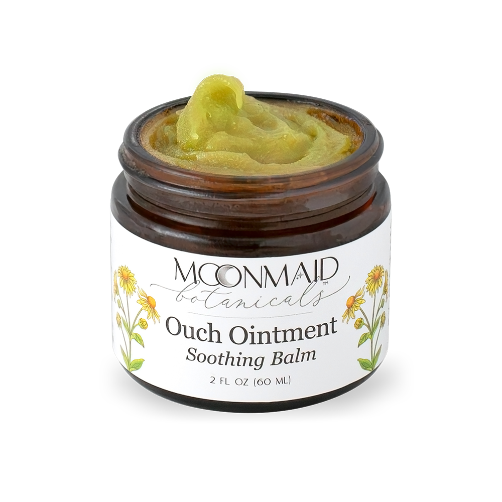 An angled close-up view of an open jar of Moonmaid Botanicals Ouch Ointment, highlighting its thick, natural green herbal salve texture.